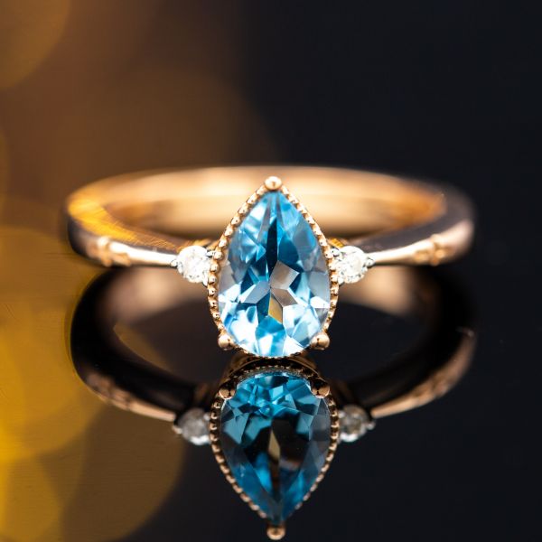 A delicately tapered 14k rose gold band with a pear cut sky blue topaz center stone.