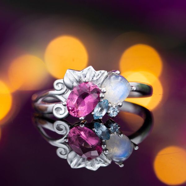A modern, asymmetric cluster ring combines moonstone, pink tourmaline, and aquamarine in a floral setting.