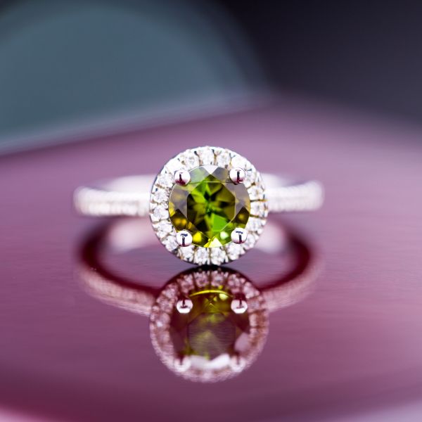 A modern engagement ring in white gold with a deep green tourmaline surrounded by a diamond halo.