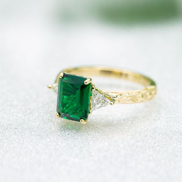 This vintage-inspired 3 stone ring features an emerald cut emerald with trillion cut diamond side stones.