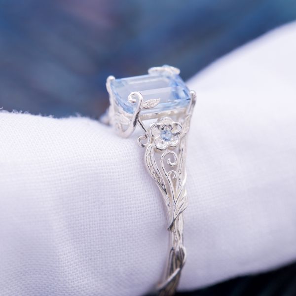 An impossibly delicate floral setting sees the vines curl up and around the emerald cut aquamarine center stone.
