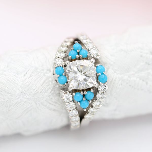 This diamond engagement ring surrounds a beautiful cushion cut diamond with turquoise accents for a distinctive twist.
