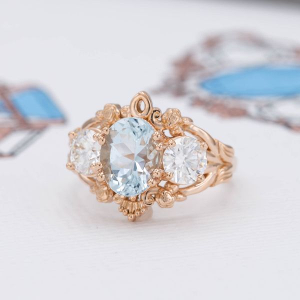 A bold, vintage-inspired engagement ring sets an aquamarine and half-carat diamonds in an intricate, floral rose gold design.