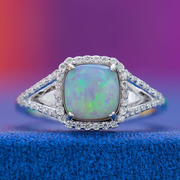 The star of this split shank engagement ring is an opal with shades of blue and green shimmering on its surface.