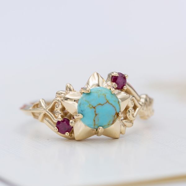 A unique engagement ring with pops of ruby contrasting with the gold-veined turquoise center stone.
