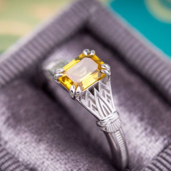 A crisp yellow sapphire (emerald cut) features in this Egyptian Revival-themed engagement ring.