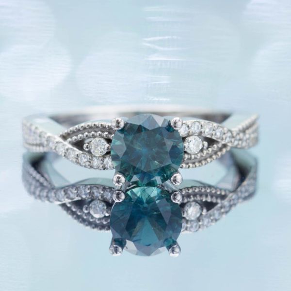 This ring's vining shank surrounds the teal blue-green sapphire center stone.