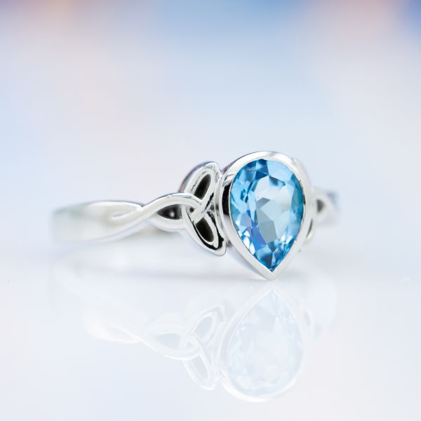 A simple, elegant design in 18k white gold with a pear cut Swiss blue topaz securely bezel set between trinity knots.