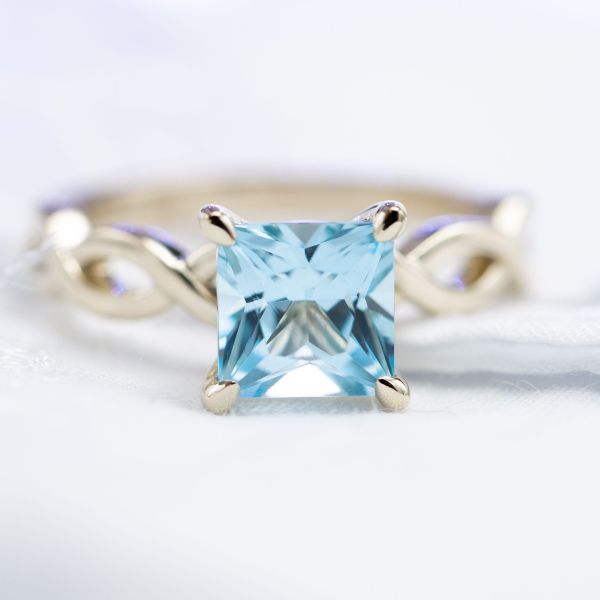 A crystal clear princess cut sky blue topaz set in a delicately vining 14k white gold shank.