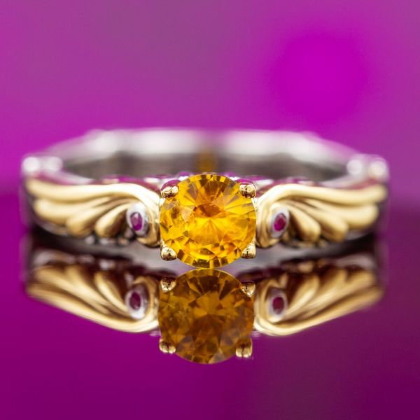 A warm orange-hued yellow sapphire is framed by gold wings in this ring.