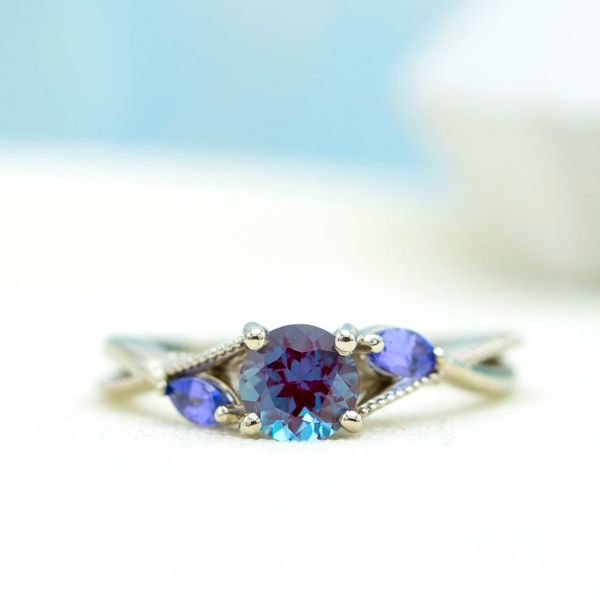 Two violet tanzanite accents in this delicate engagement ring will draw out the blue-purple hues from the alexandrite center stone in some lighting.