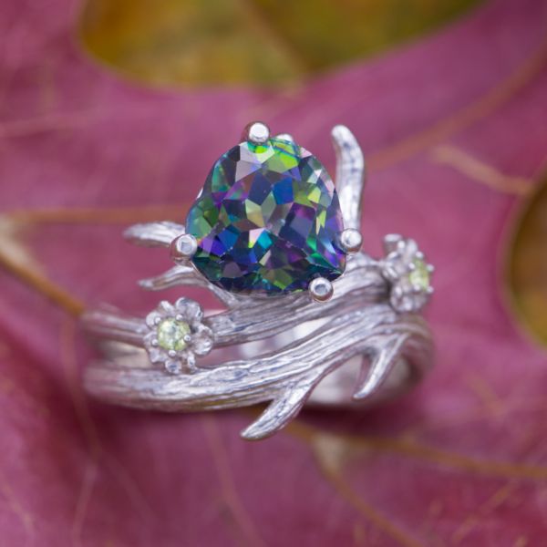 Mystic topaz is a unique, treated gem with a rainbow of colors reflecting from its facets. Here, a heart cut mystic topaz is the centerpiece for a bold, nature-inspired branch and flower ring with peridot accents.