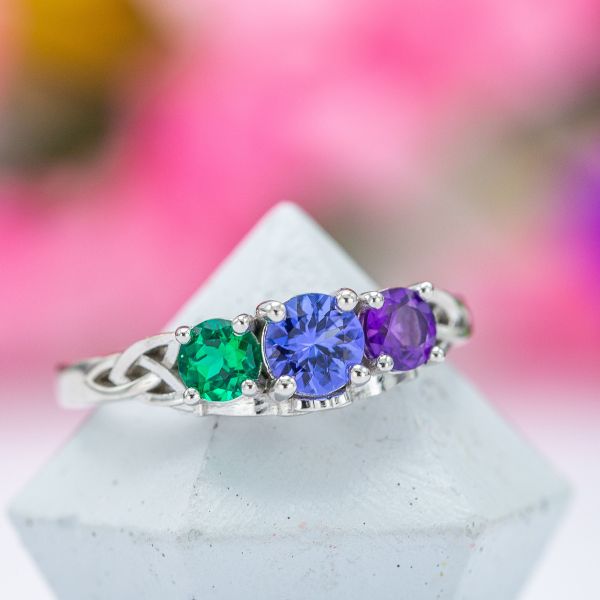A Celtic trilogy ring with amethyst and emerald around the tanzanite center stone.