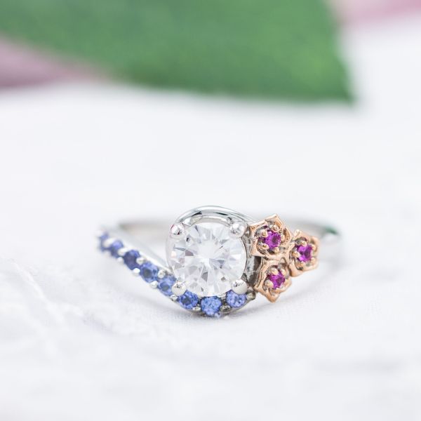 Tanzanite accents partner with pink sapphire to create an elegant floral engagement ring with a moissanite center stone.