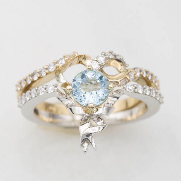 Designed to look like ribbons twisting in white and yellow gold, this engagement ring and wedding band sit together and form a heart shape around the center aquamarine.