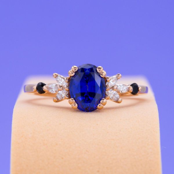 Light and dark accents add a touch of drama to this lab-created sapphire and rose gold ring. Three marquise cut diamond accents create sunburst clusters on either side of the sapphire, with an onyx capping off each end of the band.