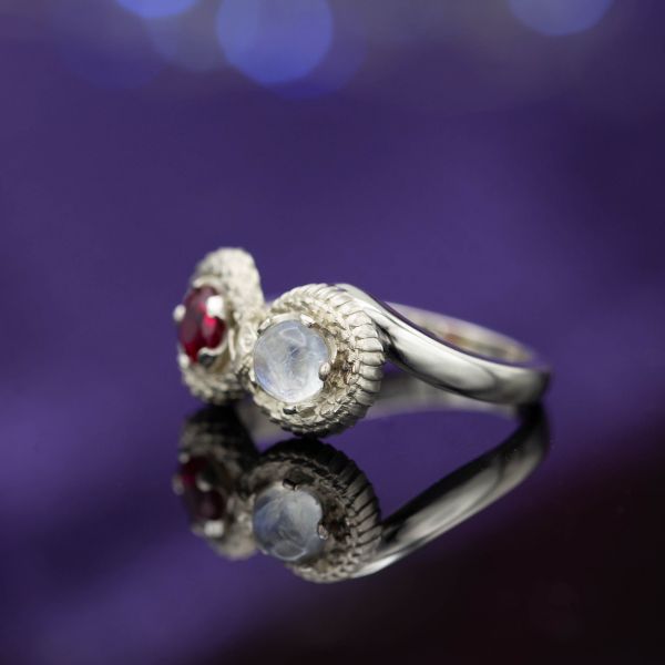 A two-stone ouroboros ring depicts a snake eating its own tail, winding an infinity symbol around a moonstone and a ruby. 