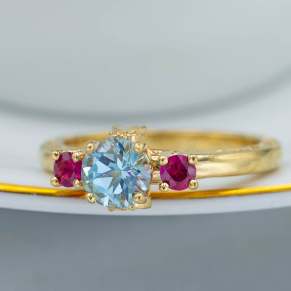 For a woman who loves colored gems and competes as a ballroom dancer, we designed this ring with sky blue topaz and ruby, featuring silhouettes of a dancing couple on the side of the setting.