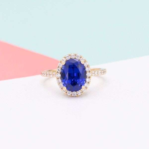 This yellow gold engagement ring offers a modern take on the classic royal ring worn by Princess Diana and Kate Middleton. An oval cut, lab-created blue sapphire sits in the center of a halo of lab diamonds, with even more bling floating down the band in a pavé setting.